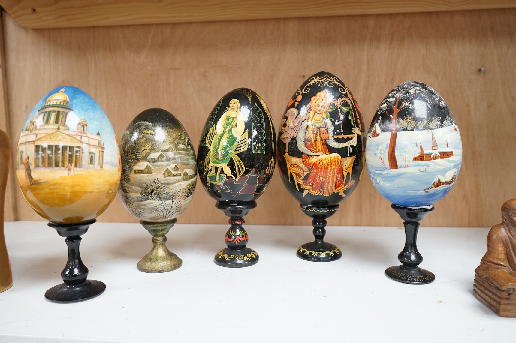 Five Russian painted and lacquered 'eggs' on stands, one inscribed in cyrillic, largest 21cm high
